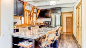 Een keuken met donkere kastjes, een centraal eiland met stoelen, een koelkast en een magnetron.