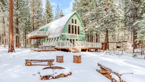 Een chalet met terras, omringd door besneeuwde grond en bomen.
