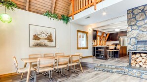 Een eetgedeelte met een houten tafel en stoelen, een keuken op de achtergrond, en een stenen muur.