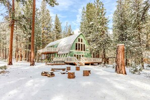 Uma cabana com telhado verde, rodeada por altas árvores de pinheiro cobertas de neve.