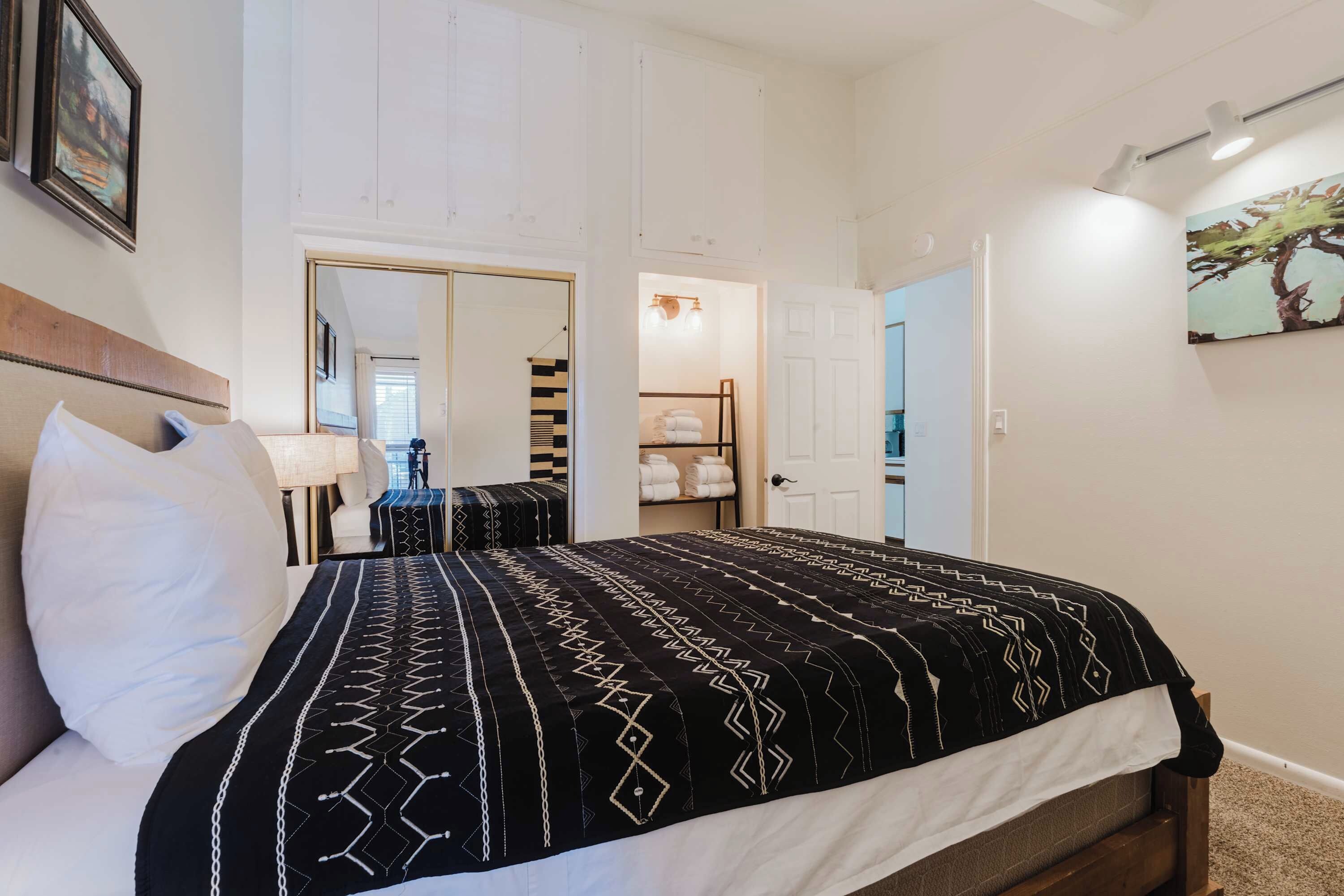 Een hotelkamer met een bed, nachtkastje, lamp, garderobe en spiegel.