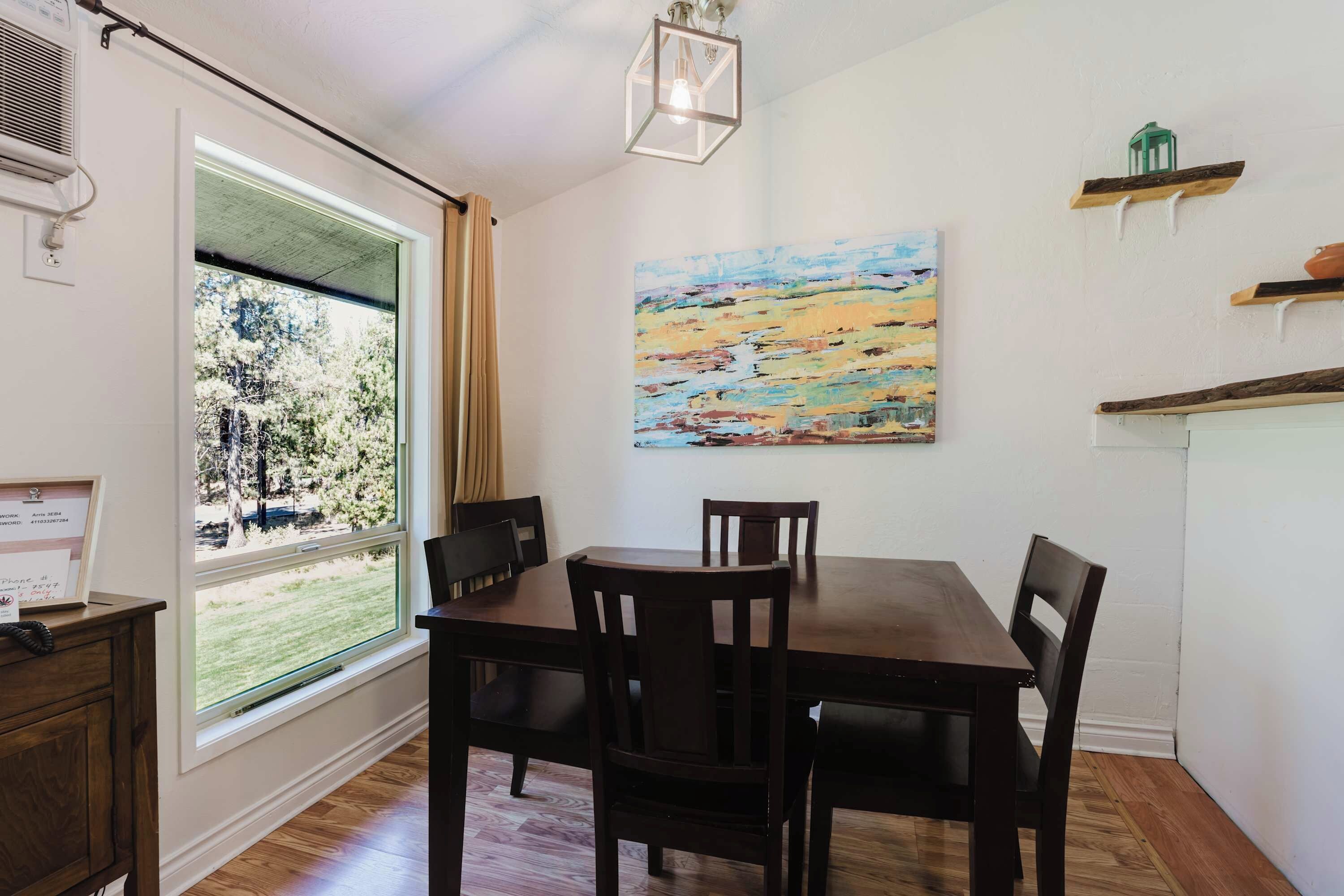 Un coin repas avec une table et des chaises, un tableau accroché au mur et une fenêtre avec des rideaux.