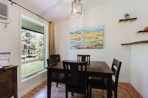 A dining area with a table and chairs, a painting on the wall, and a window with curtains.