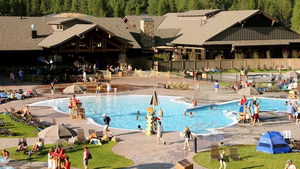 A pool area with multiple swimming pools, lounge chairs, and a wooden building with a rustic design. - Dog-Friendly Condo Steps from the Village with Balcony, WiFi & Gas Fireplace (Sunriver)