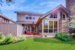 Une maison à deux étages dotée d’un patio couvert, d’une cheminée en pierre et d’une pelouse bien entretenue.