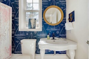 A bathroom with nautical-themed wallpaper, a white sink, a round mirror, and a toilet. - Stunning Lighthouse Replica Home with Ocean Views - Steps from the Beach (Newport)