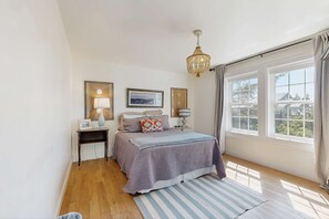 A bedroom with a bed, bedside tables, a chandelier, and large windows. - Stunning Lighthouse Replica Home with Ocean Views - Steps from the Beach (Newport)