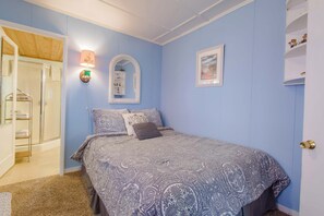 Una camera da letto con un letto, uno specchio fissato alla parete, un quadro incorniciato e una mensola con figurini.