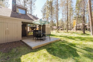 Eine Holzterrasse mit Tisch und Stühlen, ein überdachter Außenbereich und ein Gebäude mit Schornstein.