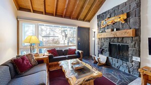 Ein gemütliches Wohnzimmer mit Kamin aus Stein, Holzbalkendecke, einer Couch mit gemusterten Kissen und einem Couchtisch.