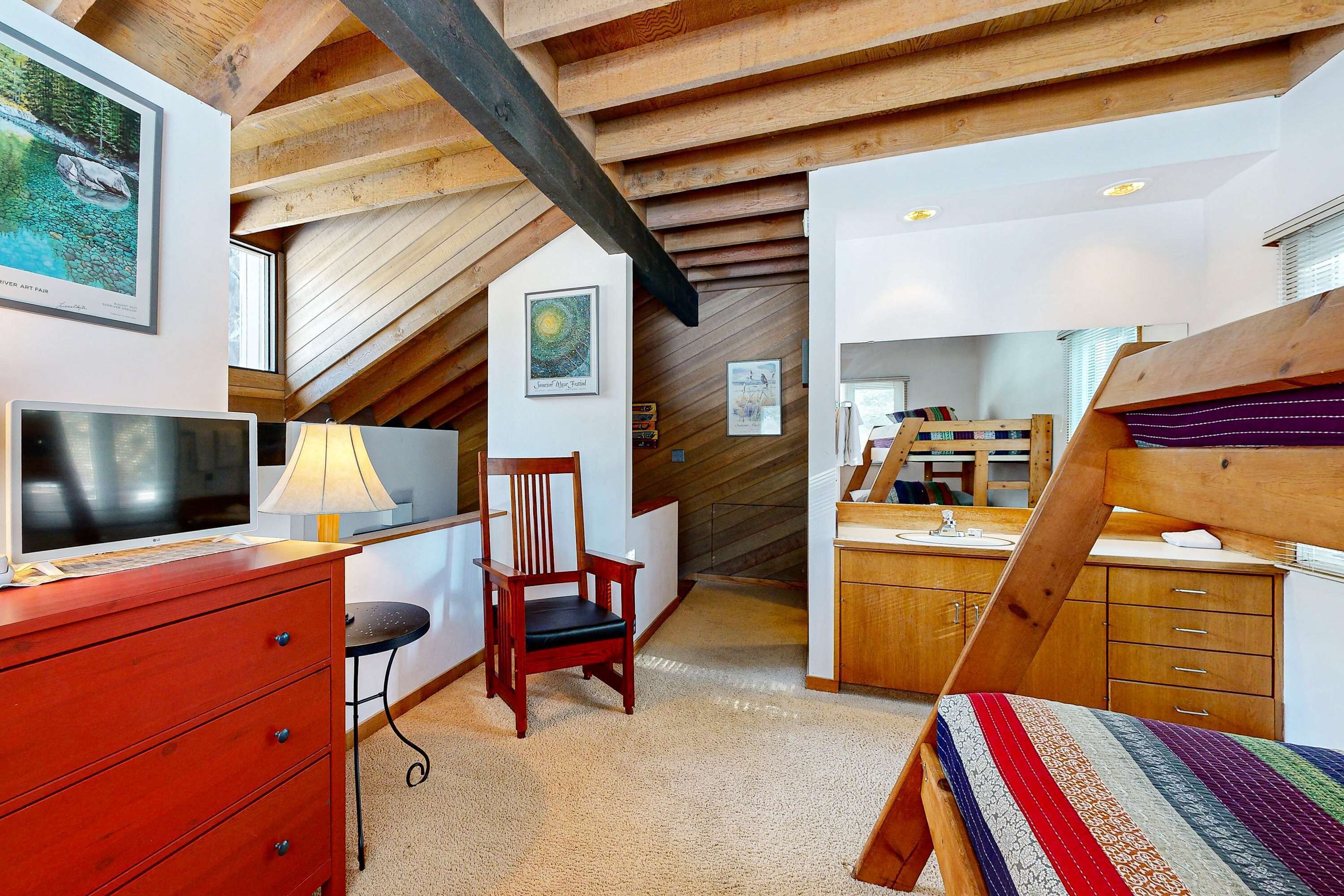 A bedroom with a sloped ceiling, wooden beams, a bed, a chair, a TV, a lamp, and a dresser.
