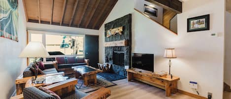 A spacious living room with a high ceiling, a stone fireplace, a television, and a cozy seating area with a sofa and coffee table.