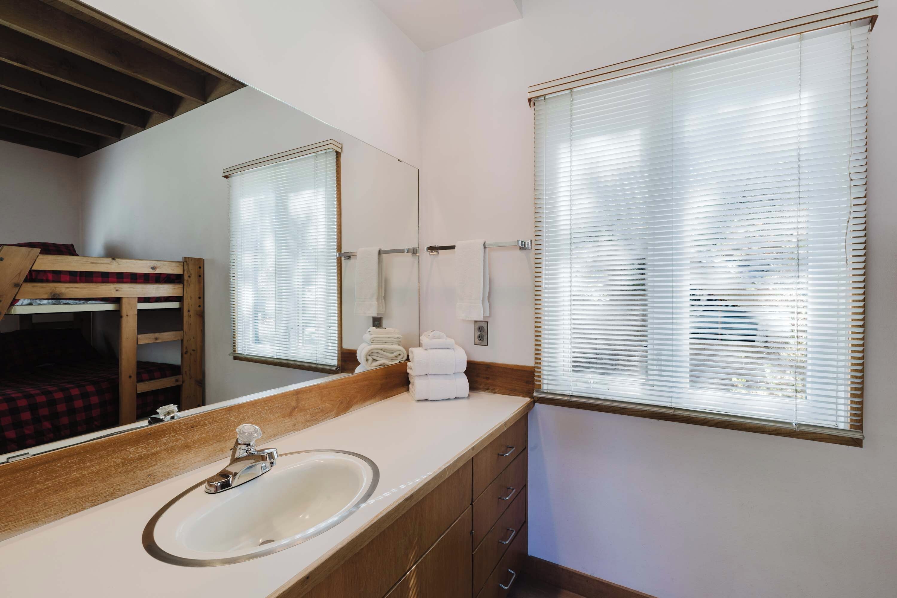 A bathroom with a sink, mirror, and window blinds.