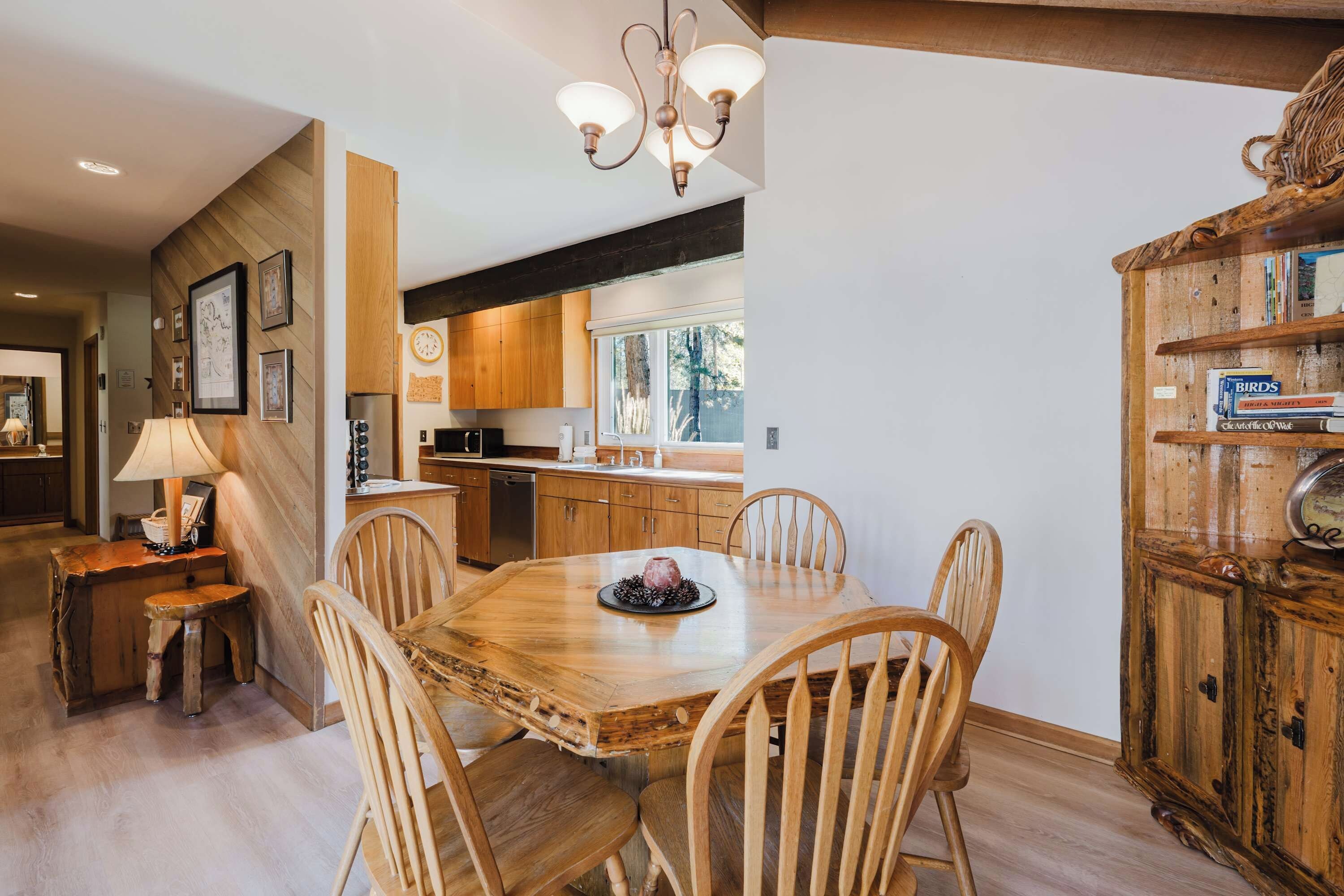 A dining area with a wooden table and chairs, a chandelier, and a rustic wooden cabinet with books.