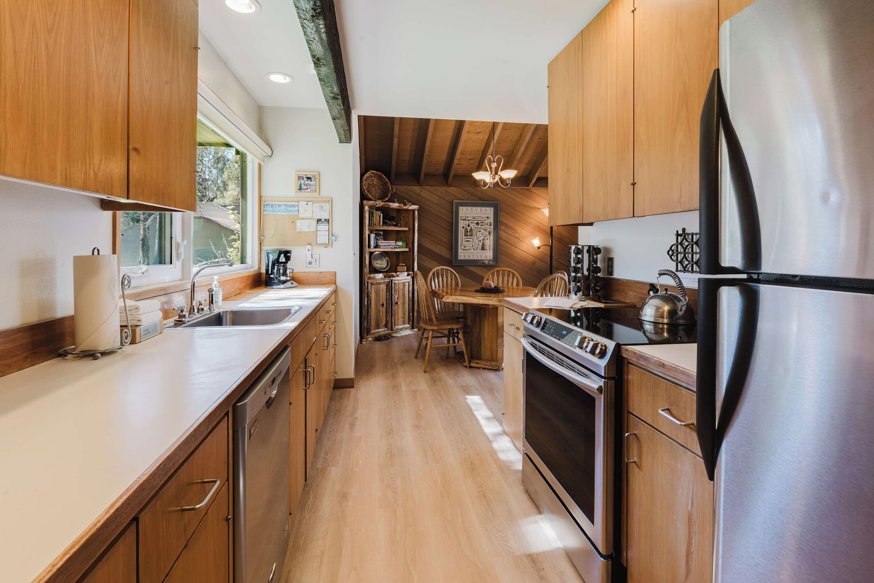 A compact kitchen with wooden cabinets, a stainless steel refrigerator, and a dining area with a wooden table and chairs.