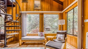 Ein gemütliches Blockhaus-Interieur mit einer Holztreppe, einem Bett mit Blick, einem Sessel und einem kleinen Tisch.