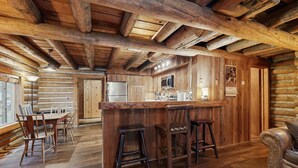 L’intérieur d’une cabane en rondins comprend un coin repas en bois, un bar avec des tabourets et une cuisine équipée d’un réfrigérateur et d’un four à micro-ondes.