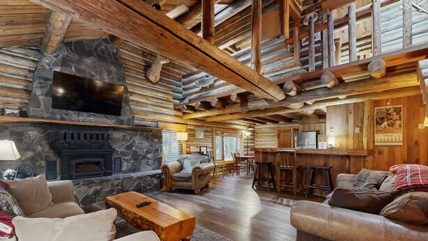 L’intérieur d’une cabane en rondins, avec une cheminée en pierre, des meubles en bois et un coin bar.