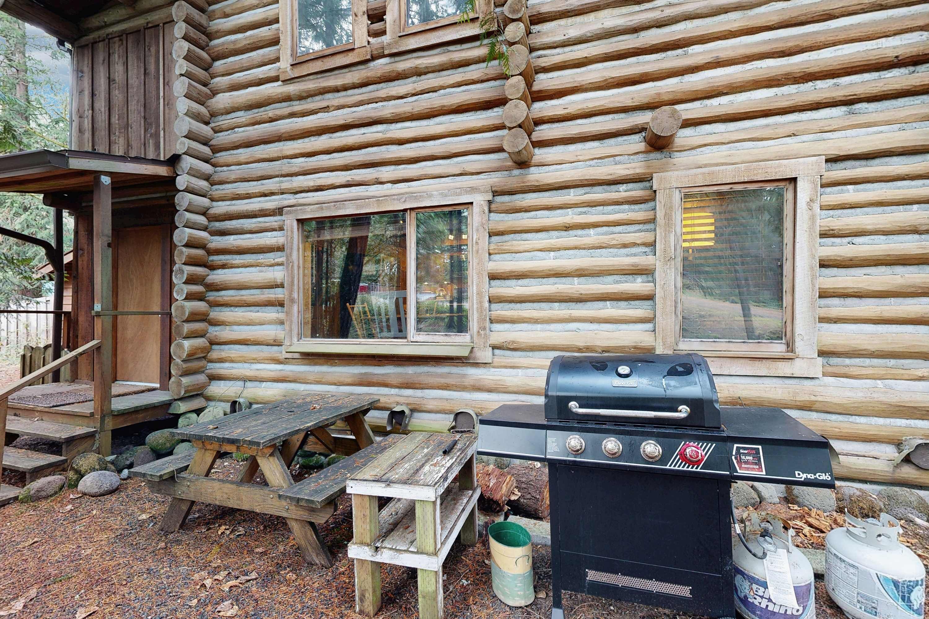 Une cabane en rondins avec un barbecue, une table de pique-nique et des marches en bois menant à une porte.