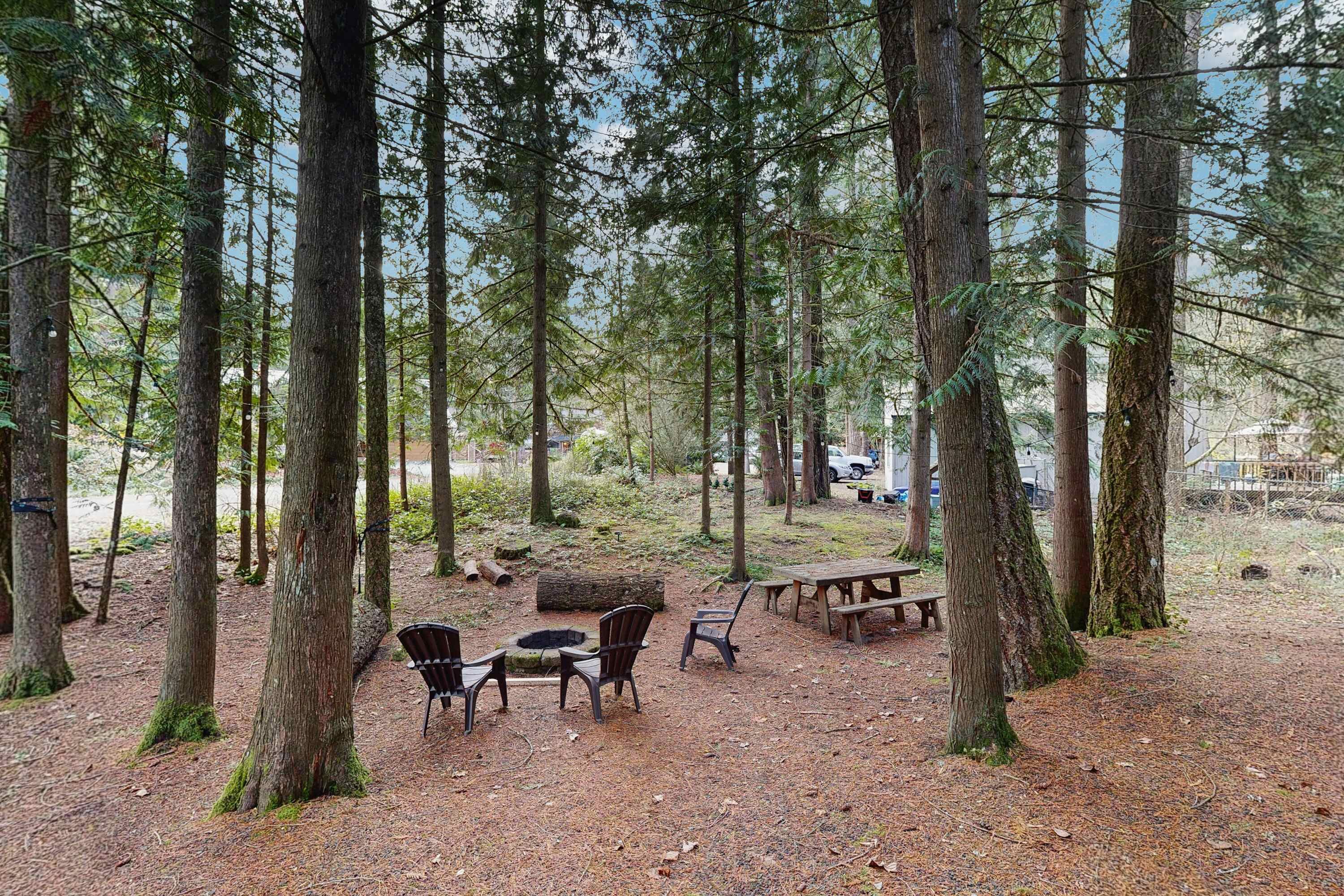 A forested area with picnic tables and chairs, surrounded by tall trees.