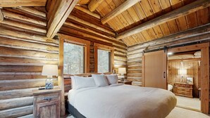Une chambre située dans une cabane en rondins, avec un grand lit, deux fenêtres, une commode en bois et un placard.