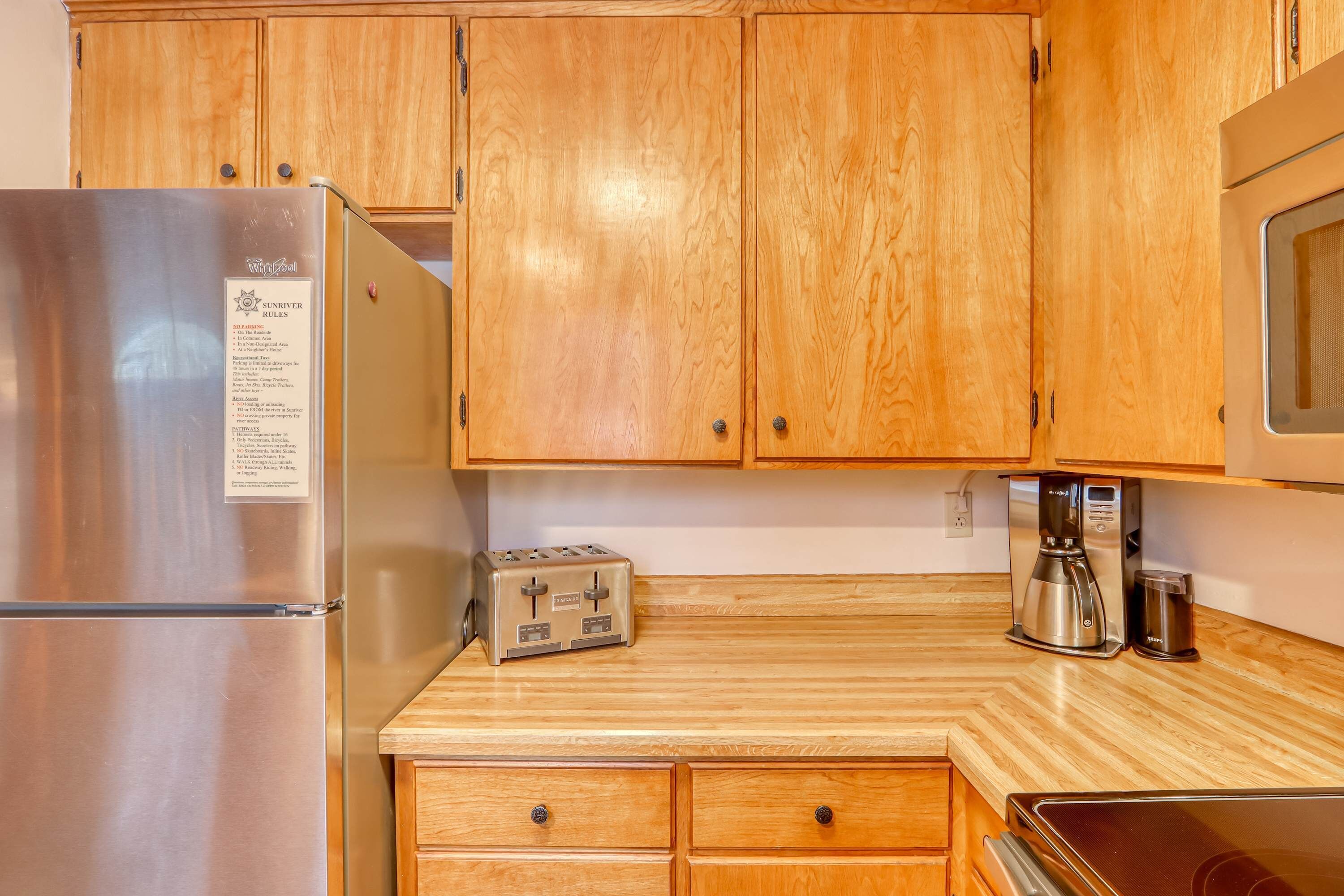 A kitchen with wooden cabinets, a stainless steel refrigerator, a toaster, a coffee maker, and a microwave.