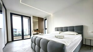 Ein modernes Schlafzimmer mit einem großen Bett, einem Nachttisch und Blick durch eine Schiebetür.