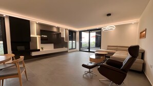 Ein modernes Wohnzimmer mit einer Couch, Sesseln, einem Couchtisch, einem Fernseher und einem Kamin.