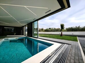 A modern indoor swimming pool with clear blue water, large windows, and a view of a well-maintained lawn. - Luxury Villa Admiria Split - Heated Indoor Pool & Stunning Terrace (Split)