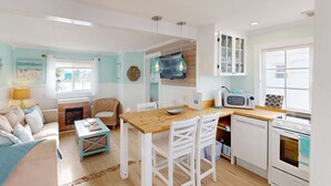 Uma sala de estar acolhedora, com um sofá, uma mesa de jantar de madeira e uma área de cozinha com micro-ondas e forno.