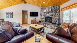 A cozy living room with leather sofas, a wooden coffee table, a stone fireplace, and a flat-screen TV. - Dog-Friendly Sunriver Home with Fireplace, Deck & Central AC (Sunriver)