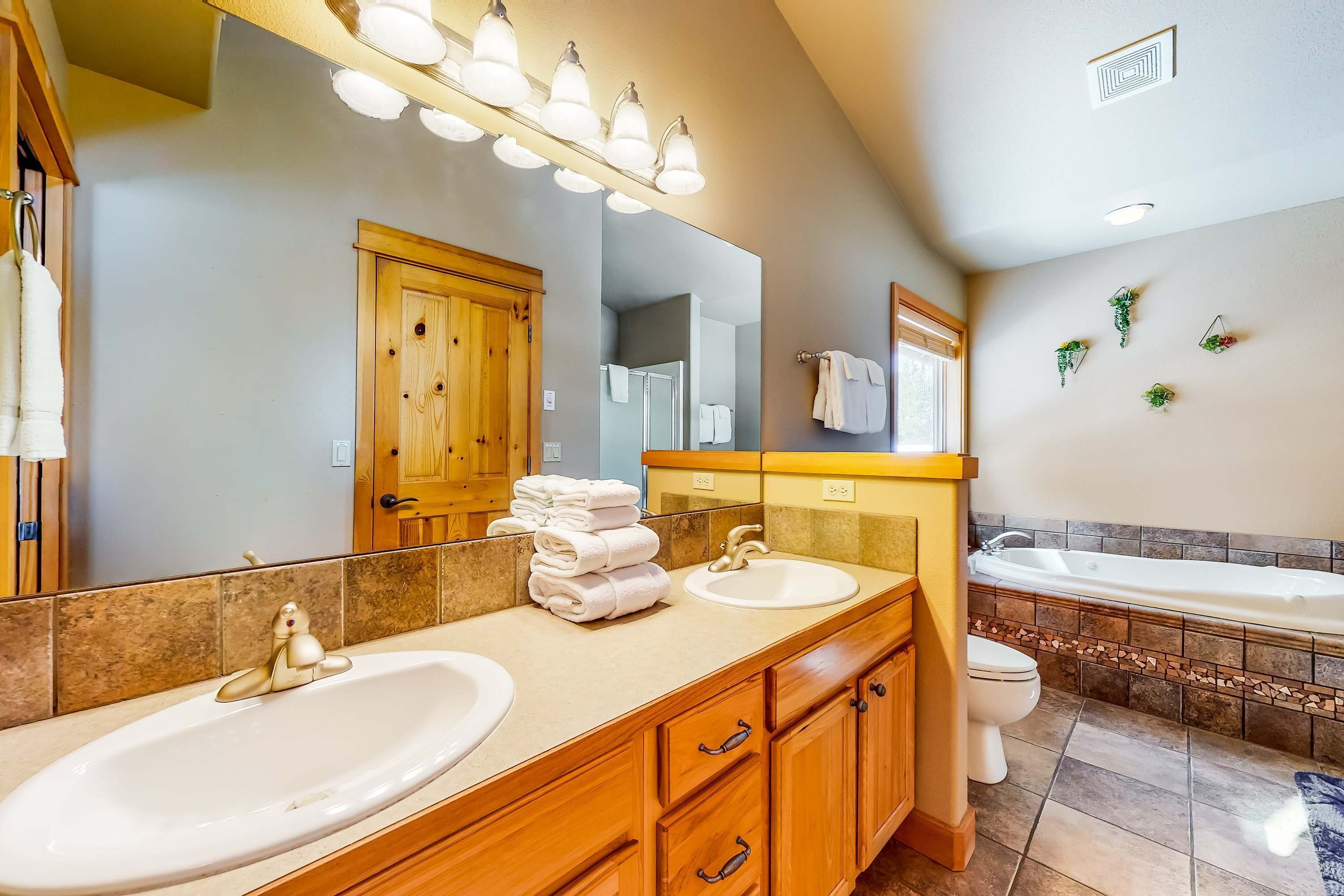 Un baño con dos lavabos, una bañera, armarios de madera y un espejo grande.