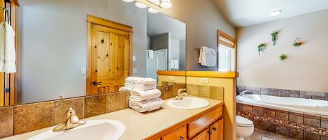 Un baño con dos lavabos, una bañera, armarios de madera y un espejo grande.