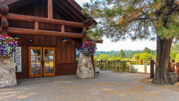 Eine Holzhütte mit Steinpfeilern, einer Holzterrasse und Blick auf Bäume und Hügel.