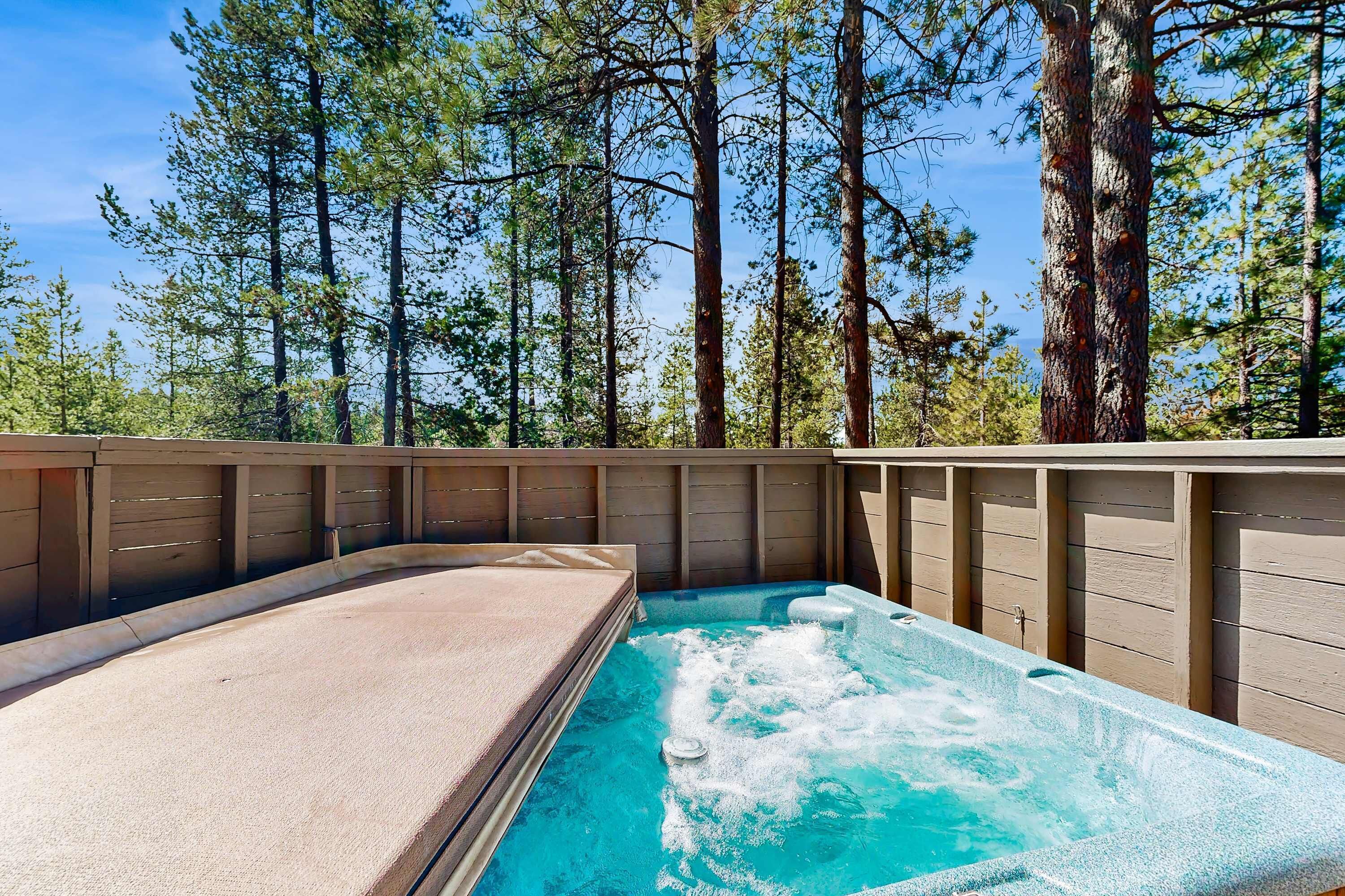 A hot tub with a wooden deck and a view of tall pine trees.