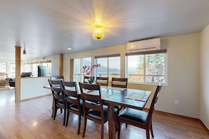 A dining area with a wooden table and chairs, large windows, and an air conditioning unit.
