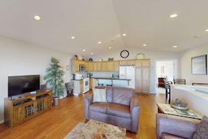 A living room with a TV, leather sofa, and a dining area with chairs and a table.
