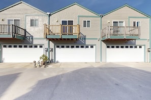 A two-story residential building with a garage, a balcony on the second floor, and a small tree in the driveway.