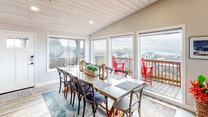 A dining area with a long table, chairs, and large windows offering a view. - Dreamy Coastal Gem Near the Beach with Ocean View, Game Room, & a Private Hot Tub (Newport)