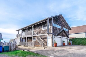 A two-story wooden house with a balcony, a garage, and a fenced yard. - Dreamy Coastal Gem Near the Beach with Ocean View, Game Room, & a Private Hot Tub (Newport)