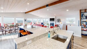 A spacious kitchen with a large island, a dining area with bar stools, and a living room with a red sofa. - Dreamy Coastal Gem Near the Beach with Ocean View, Game Room, & a Private Hot Tub (Newport)