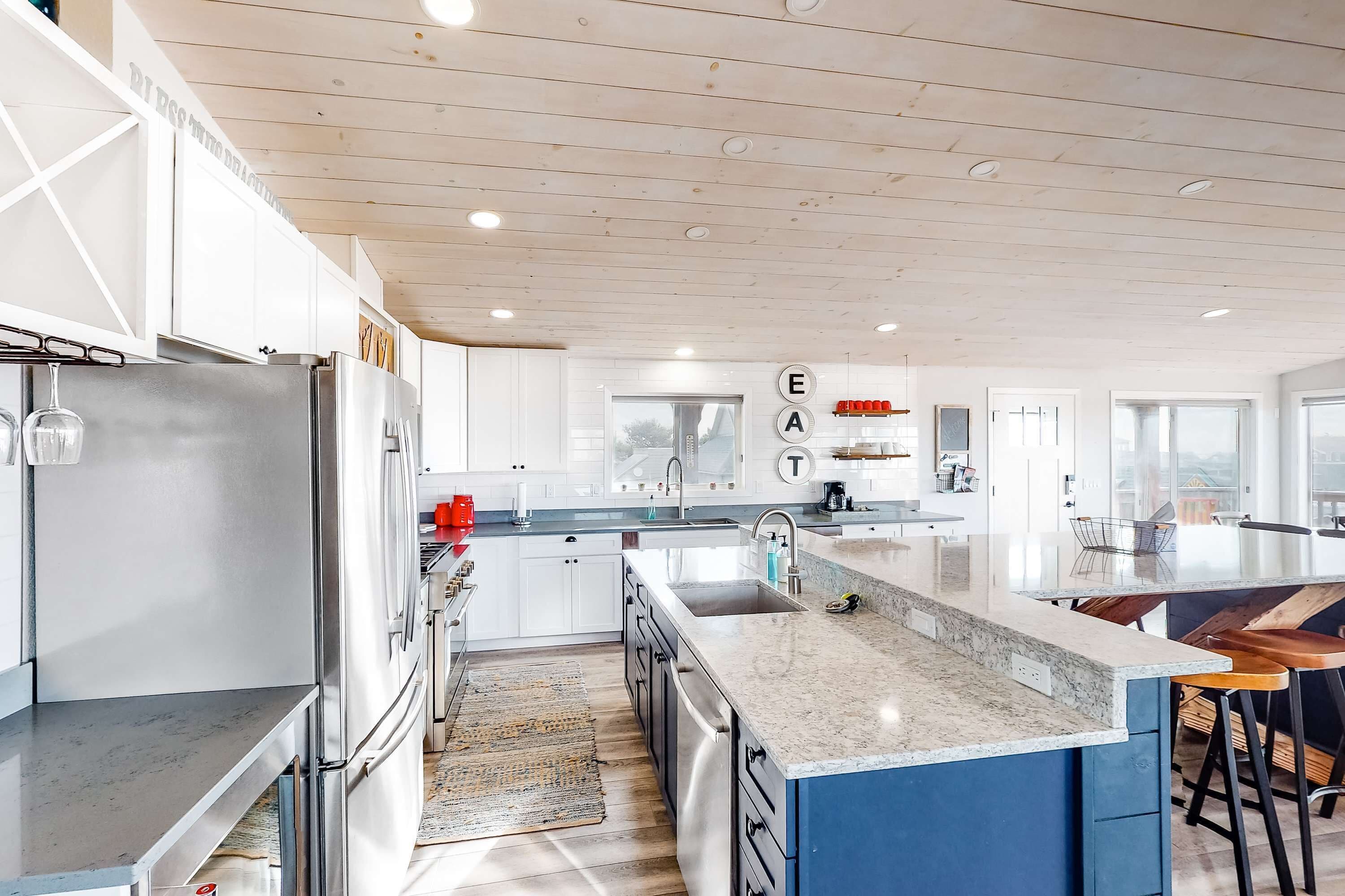 A modern kitchen with white cabinets, stainless steel appliances, a marble countertop, and a blue accent wall.