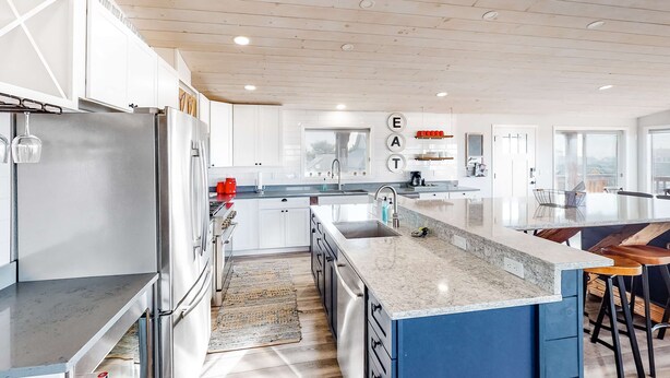 A modern kitchen with white cabinets, stainless steel appliances, a marble countertop, and a blue accent wall. - Dreamy Coastal Gem Near the Beach with Ocean View, Game Room, & a Private Hot Tub (Newport)