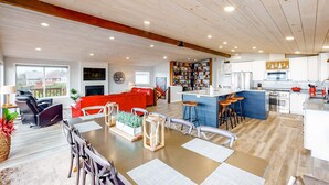 A spacious living area with a dining table, red sofa, and kitchen area with bar stools. - Dreamy Coastal Gem Near the Beach with Ocean View, Game Room, & a Private Hot Tub (Newport)