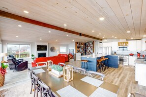 A spacious living area with a dining table, red sofa, and kitchen area with bar stools. - Dreamy Coastal Gem Near the Beach with Ocean View, Game Room, & a Private Hot Tub (Newport)