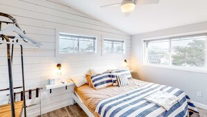 A bedroom with a bed, bedside tables, a ceiling fan, windows, and a view of the outside. - Dreamy Coastal Gem Near the Beach with Ocean View, Game Room, & a Private Hot Tub (Newport)