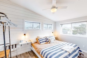 A bedroom with a bed, bedside tables, a ceiling fan, windows, and a view of the outside. - Dreamy Coastal Gem Near the Beach with Ocean View, Game Room, & a Private Hot Tub (Newport)