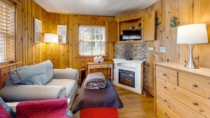 A cozy cabin-style room with wooden walls, a fireplace, a television, and a bed with striped bedding. - Dog-Friendly Beach Condo with Free WiFi - Close to Beach (Cannon Beach)