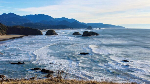 A coastal landscape with mountains, a beach, and rocky outcrops in the water. - Dog-Friendly Beach Condo with Free WiFi - Close to Beach (Cannon Beach)