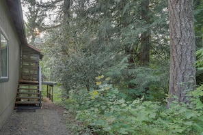 A wooden house with a porch, surrounded by dense forest. - Creekside cabin with water view, deck, jetted tub & game room - near Mt Hood (Rhododendron)